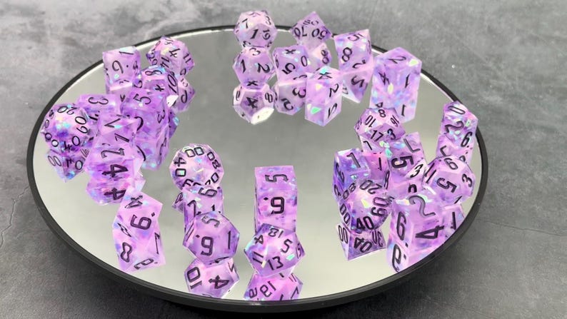 Glimmer and Glow purple resin dice with black numbers and iridescent inclusions on a mirrored tray