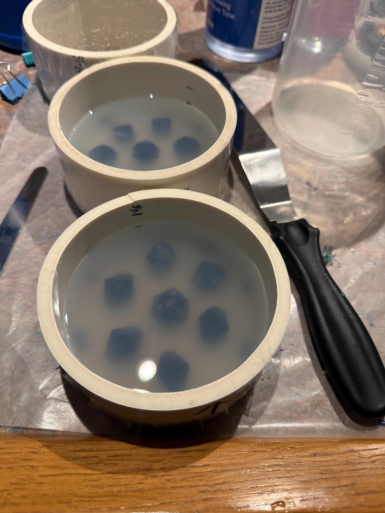 Two round mold housings filled with translucent silicone around dice masters